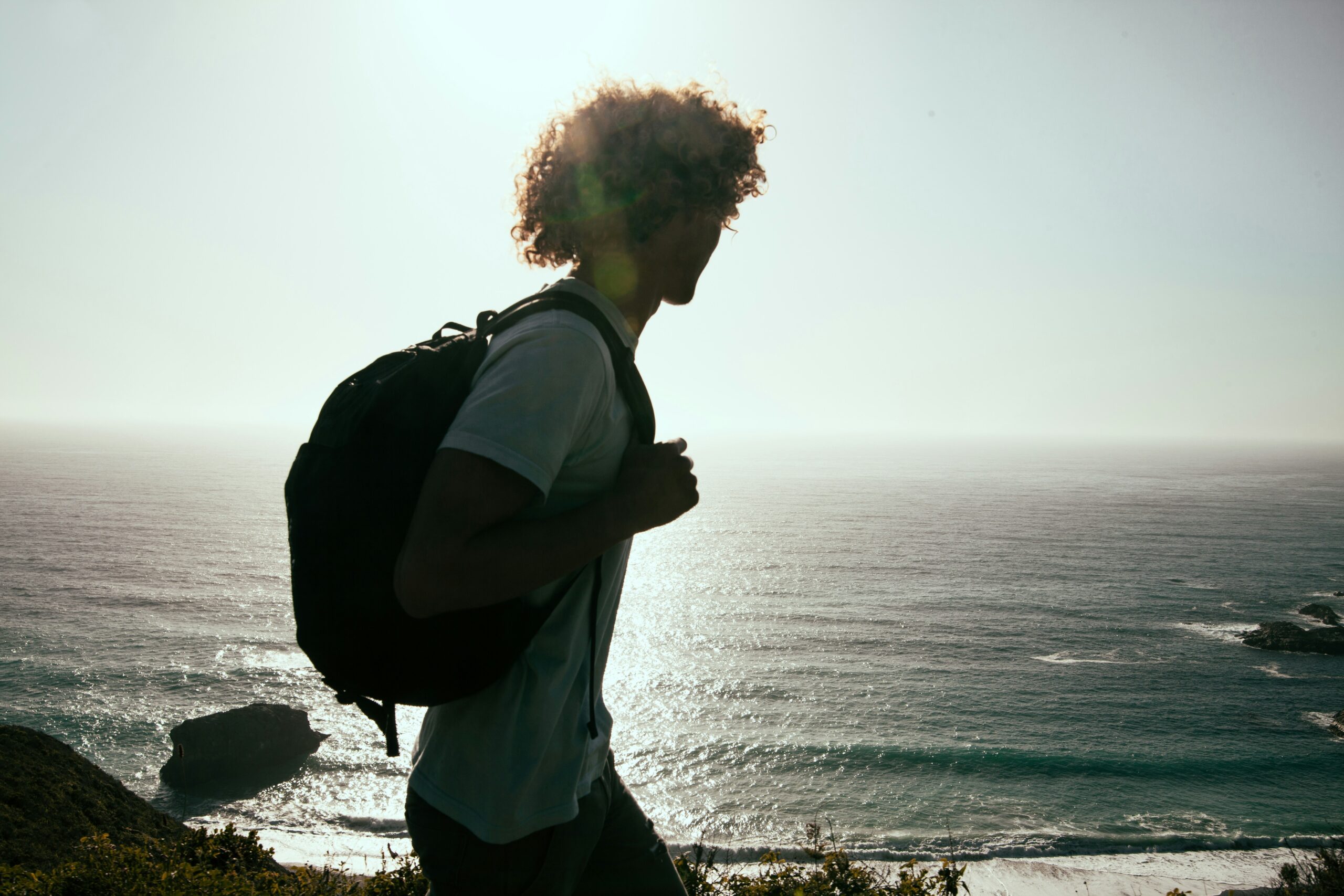 Teen boy wearing a backpack and walking by the ocean