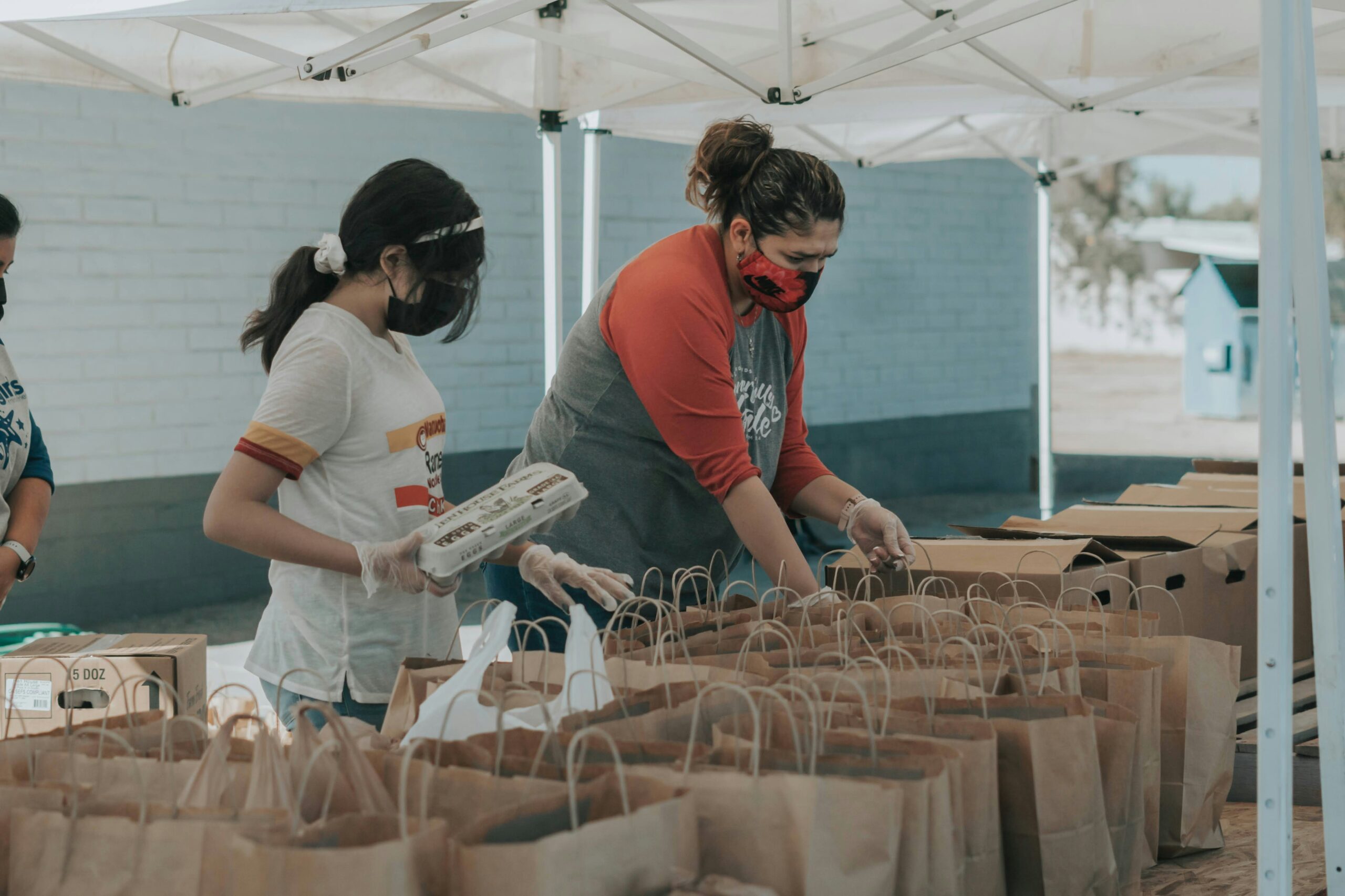 Two volunteers packing food into brown paper bags