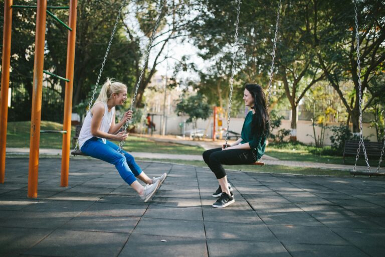 Two women laughing on park swings